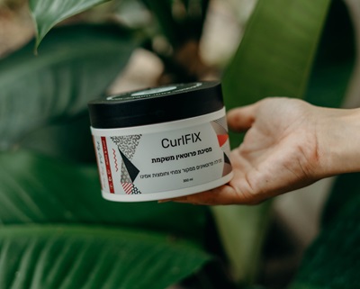 יד מחזיקה את מסכת פרוטאין CurlFIX ומאחור יש מלא צמחייה ירוקה